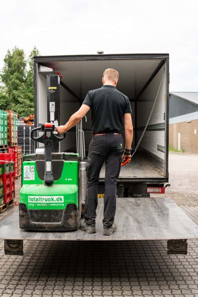 Medarbejder læsser varer i lastbilen med palleløfter